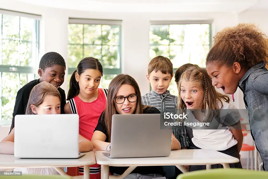 Grundschulkinder arbeiten mit Laptops im Unterricht, begleitet von ihrer Lehrkraft