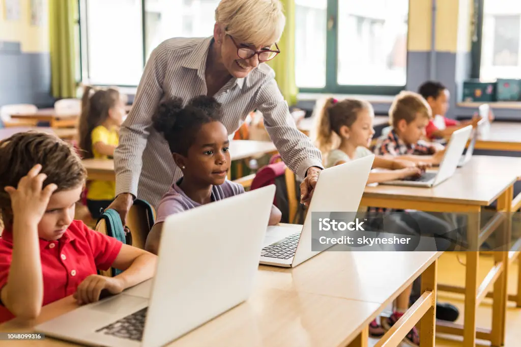 Lehrkraft unterstützt Schüler an Computern im Unterricht